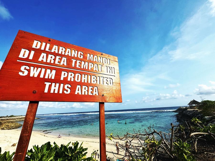 Panneau d'interdiction de baignade devant une plage turquoise
